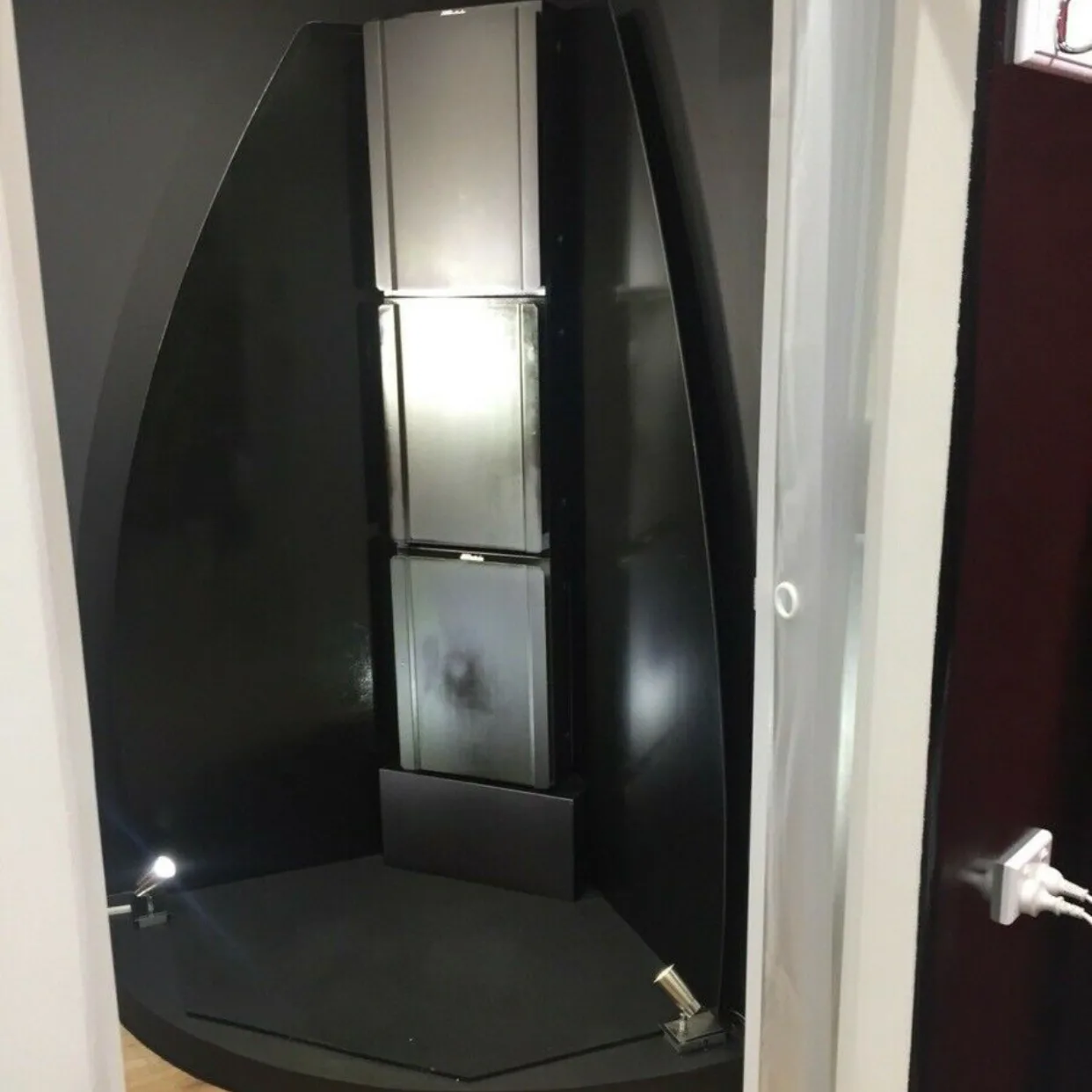 The stand-up spray-tan booth at Beauty B — a gloss-black booth with central silver spray column lit from within, set in its own alcove
